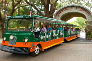 Orange and green trolley, driving through coquina gates that read Fountain of Youth