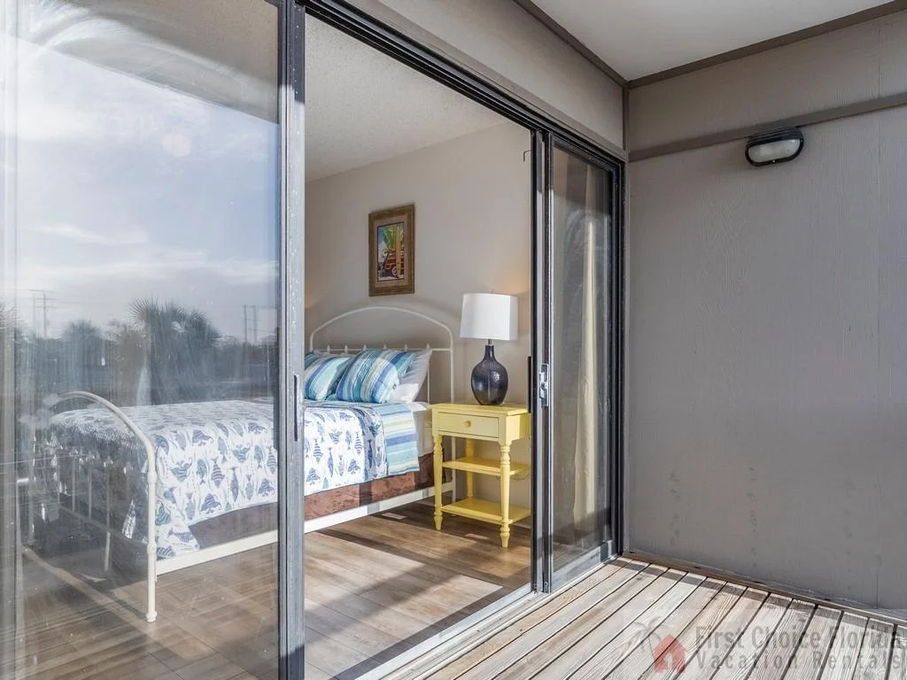 Master bedroom with white metal bed frame, seashell-patterned bedding, yellow nightstand, and balcony access.