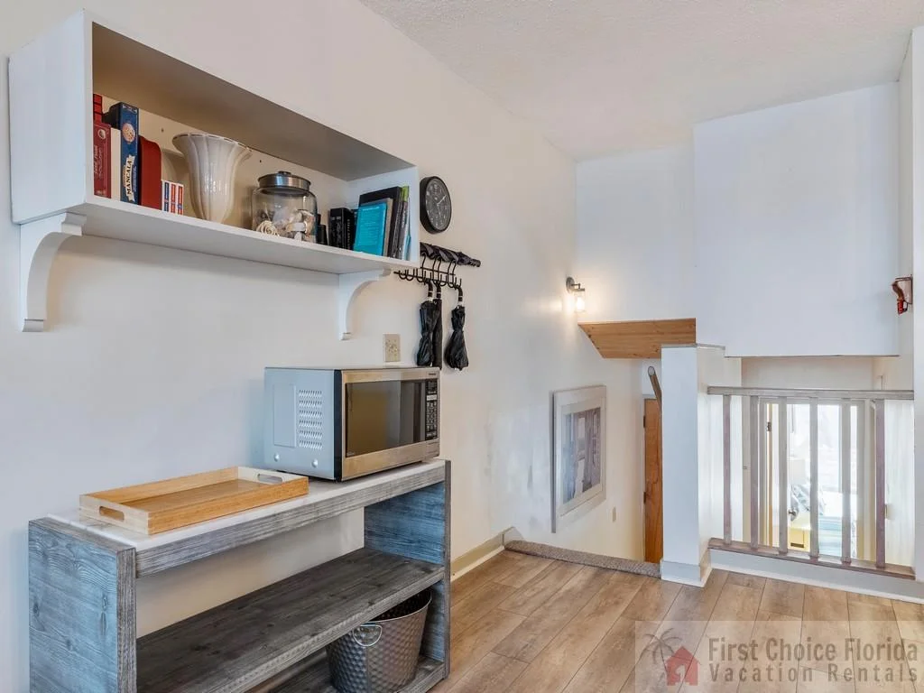Hallway nook with a gray wood console holding a microwave, a wooden tray, and a white wall shelf above.