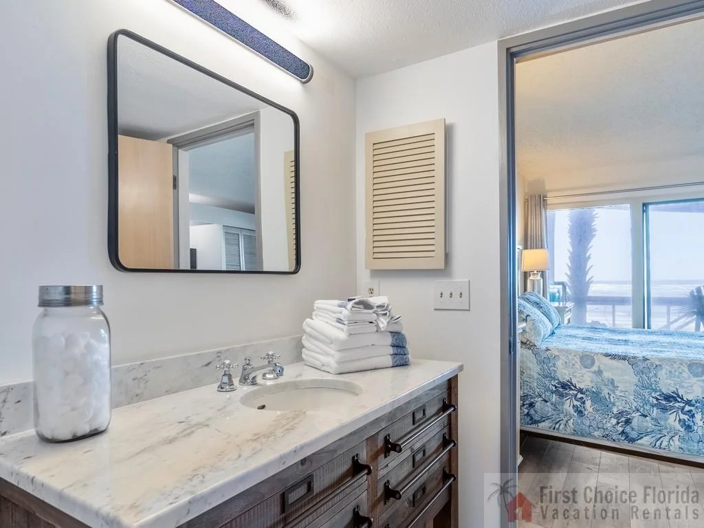 Bathroom vanity with marble countertop, stacked white towels, and a jar of cotton balls next to a mirror.