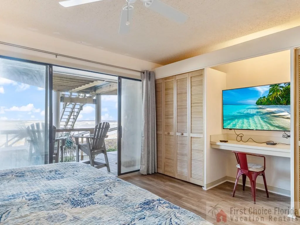 Master bedroom with wood-look flooring, louvered closet doors, and sliding glass doors opening to a balcony with ocean views.