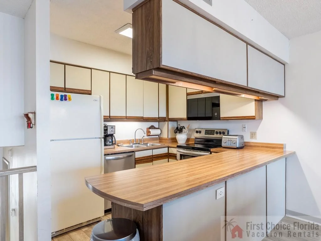 Kitchen with wood grain laminate countertops, white upper cabinets, and stainless steel appliances including dishwasher and stove.