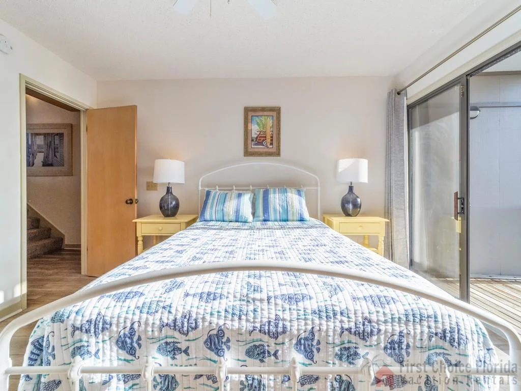 Master bedroom features a white metal bed frame, blue fish-patterned bedding, yellow nightstands, and sliding glass doors to a balcony.