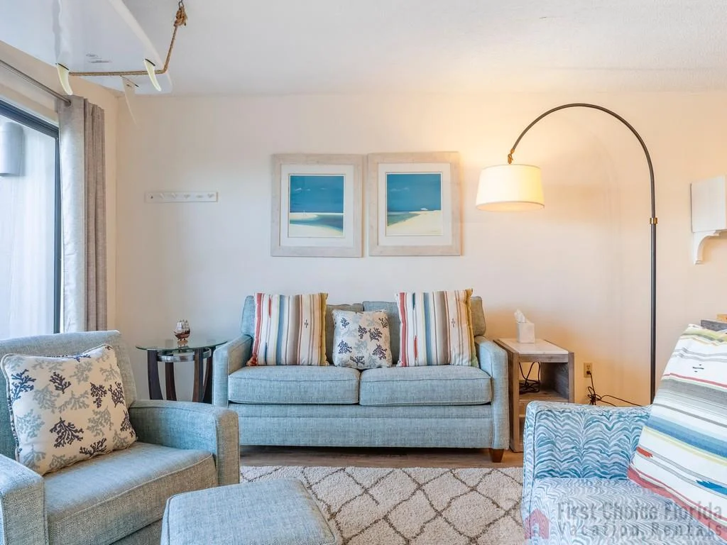 Seating area with light blue sofa, patterned cushions, glass side table, and arched floor lamp.