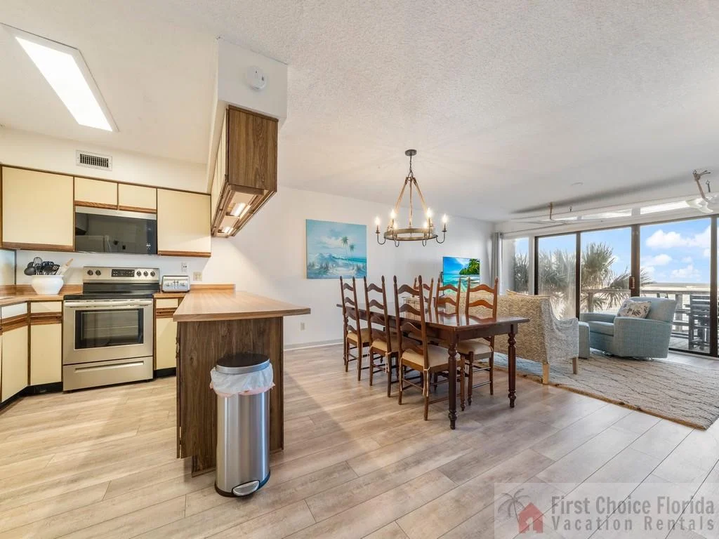 Dining area with wooden ladder-back chairs and chandelier, next to a kitchen featuring cream cabinets and stainless appliances.