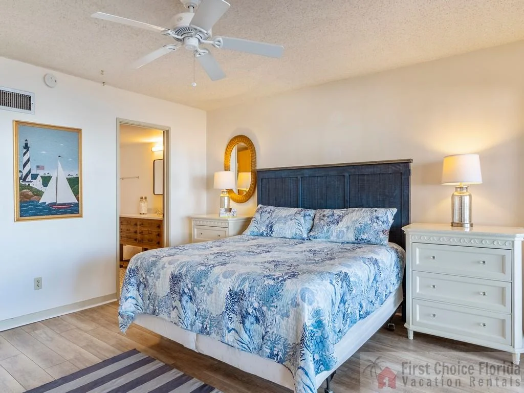 Master bedroom with a dark wood headboard, blue coral-patterned bedding, white nightstands, and lamps.