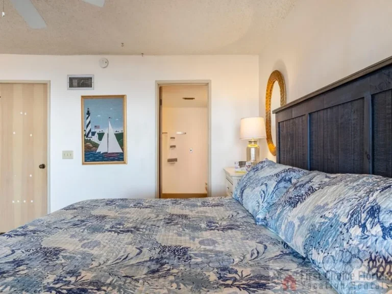 Master bedroom with dark wood headboard, seashell-patterned bedding, woven mirror, and lamp on white nightstand.