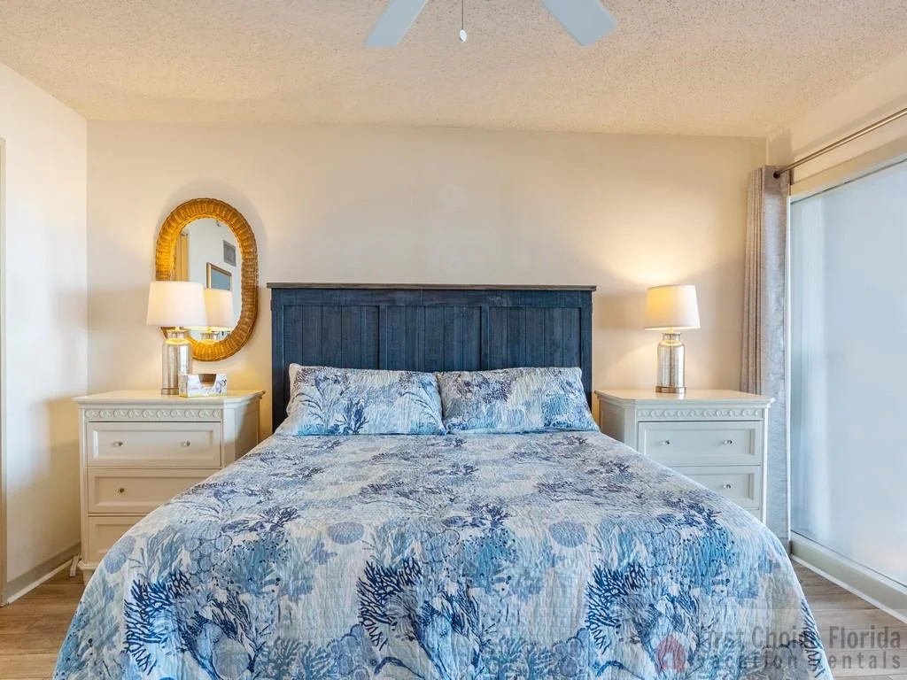 Master bedroom features a dark wood headboard, patterned blue bedding, matching white nightstands, and lamps.