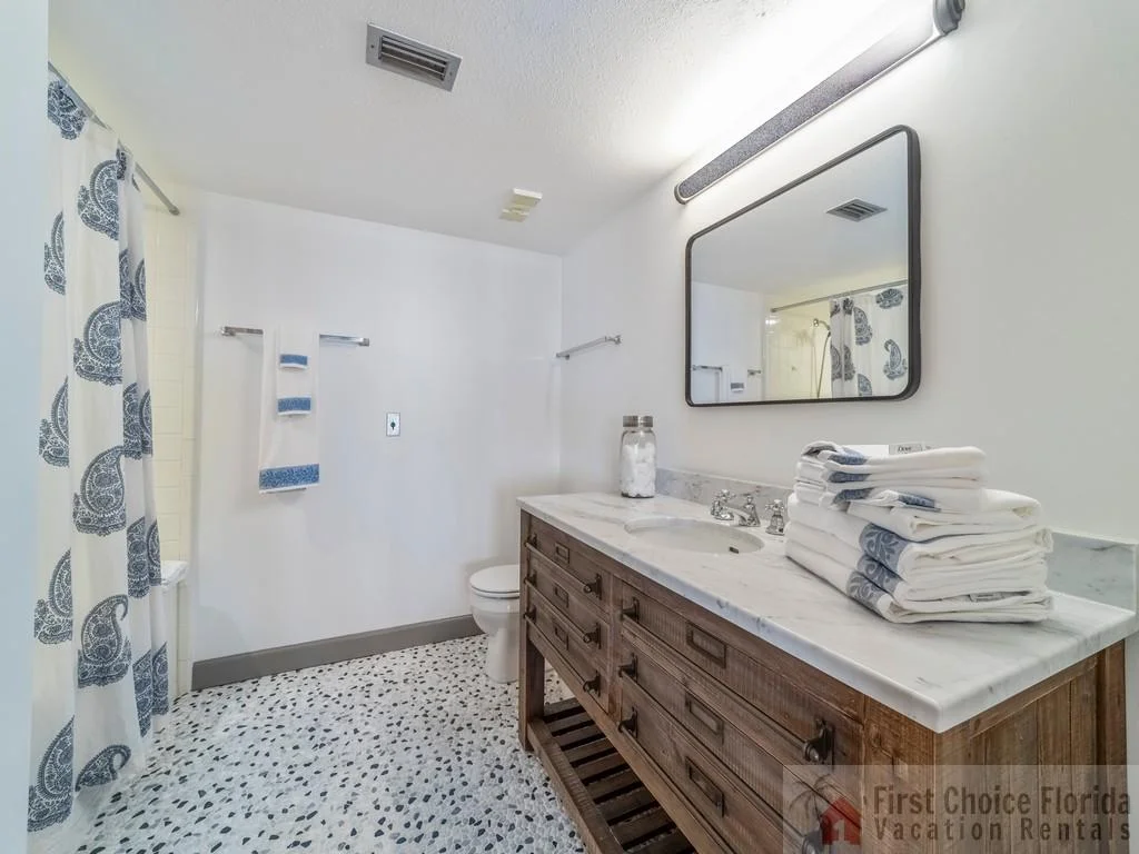 Bathroom with a wooden vanity topped by white marble, a large mirror, and terrazzo-style flooring.