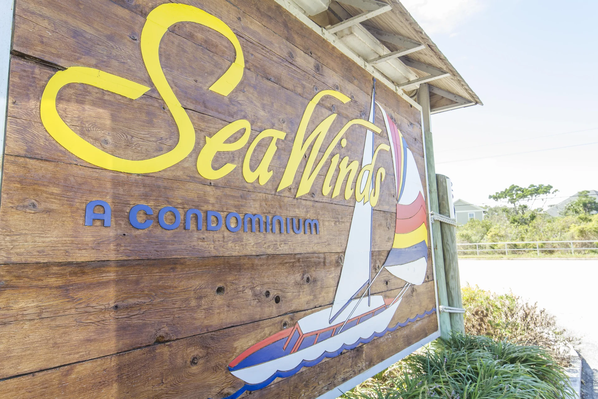 Large wooden sign with yellow and blue lettering and a colorful sailboat graphic marks the condominium entrance.