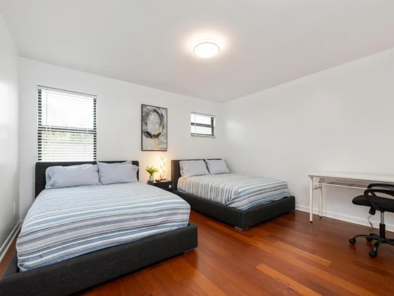 Two queen beds with striped linens sit on warm hardwood floors beneath abstract wall art.