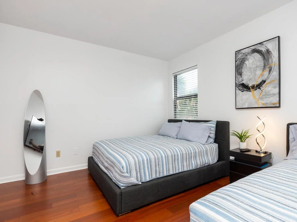 Two beds with striped bedding flank a black nightstand topped by a modern sculptural lamp and plant.