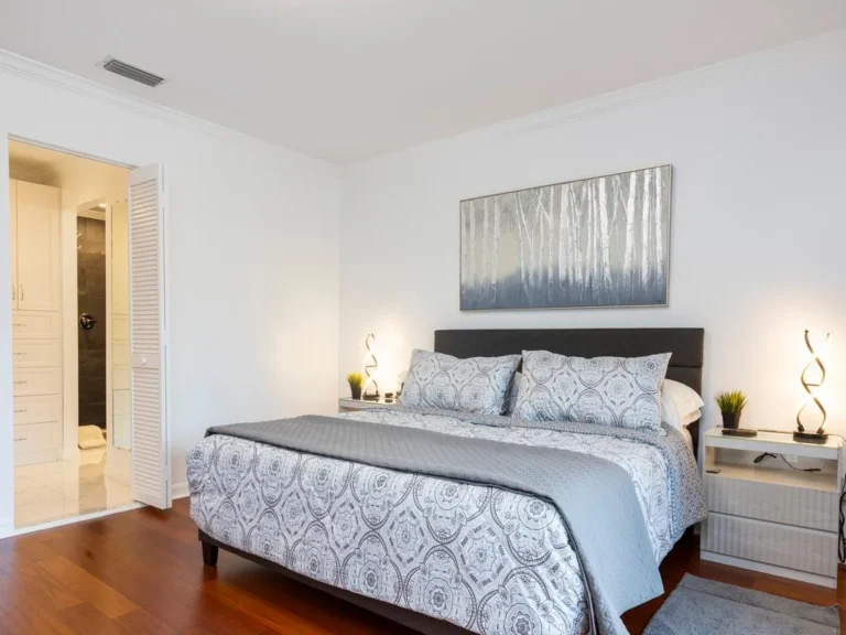 King bed with patterned bedding sits between two nightstands topped with sculptural lamps and plants.