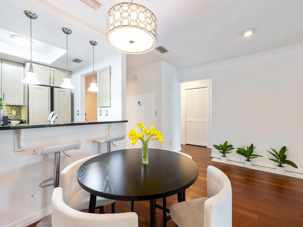 Round black dining table with four white upholstered chairs under a drum pendant light.