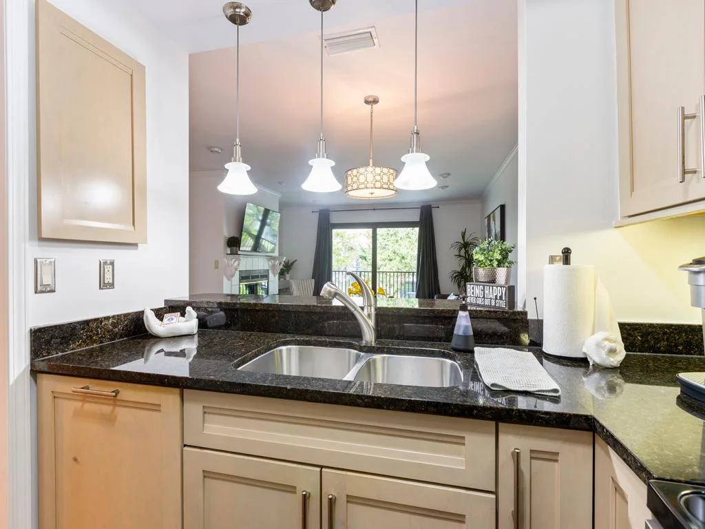 Granite countertops with double stainless steel sink under three glass pendant lights in the kitchen area.