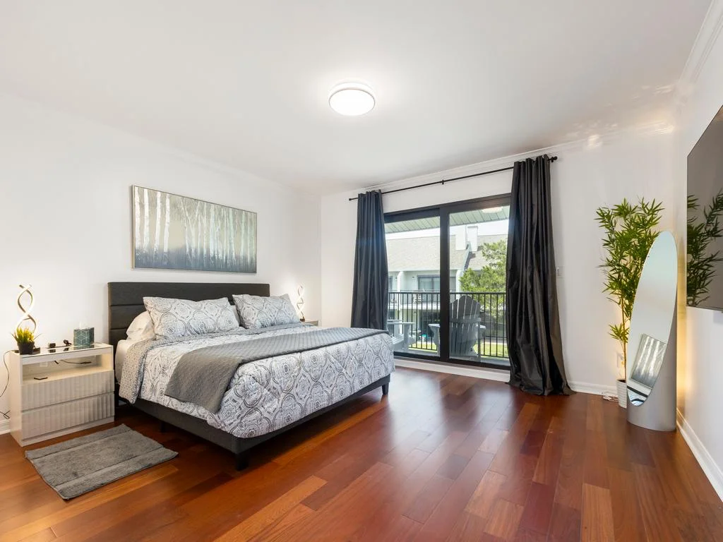 King bed with patterned bedding faces glass doors leading to a balcony, dark curtains framing the view.