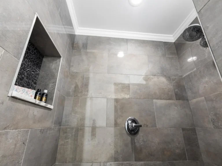 Shower area with large gray ceramic tiles, built-in niche with black pebble accent, and chrome fixtures.