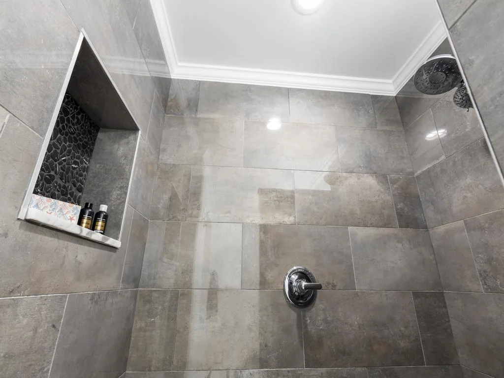Shower area with large gray ceramic tiles, built-in niche with black pebble accent, and chrome fixtures.