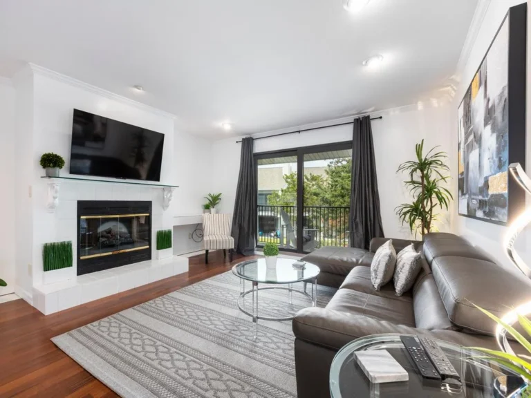 Leather sectional with patterned pillows faces a white-tiled fireplace beneath a wall-mounted TV.