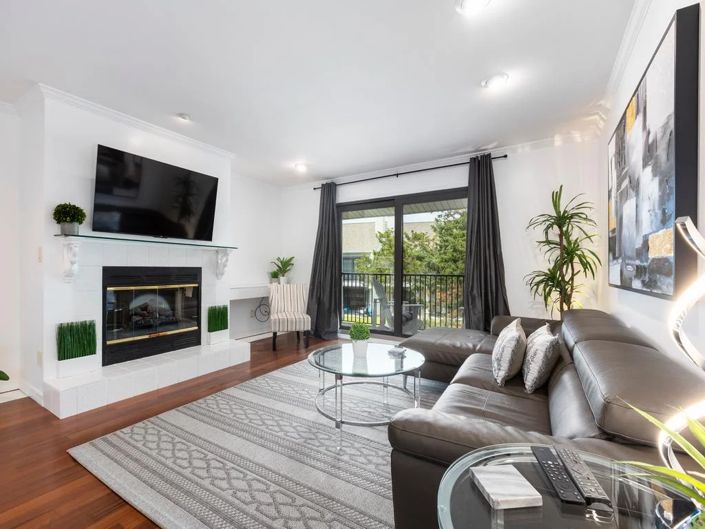 Leather sectional with patterned pillows faces a white-tiled fireplace beneath a wall-mounted TV.