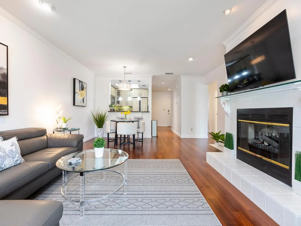 Glass coffee table and gray leather sectional anchor the living room, with a tiled fireplace and wall-mounted TV.