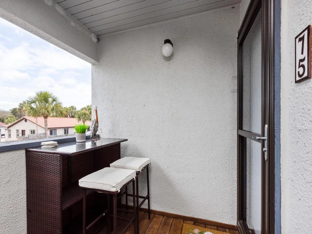 Entrance balcony with dark wicker bar table, cushioned stools, and views of palm trees and rooftops.