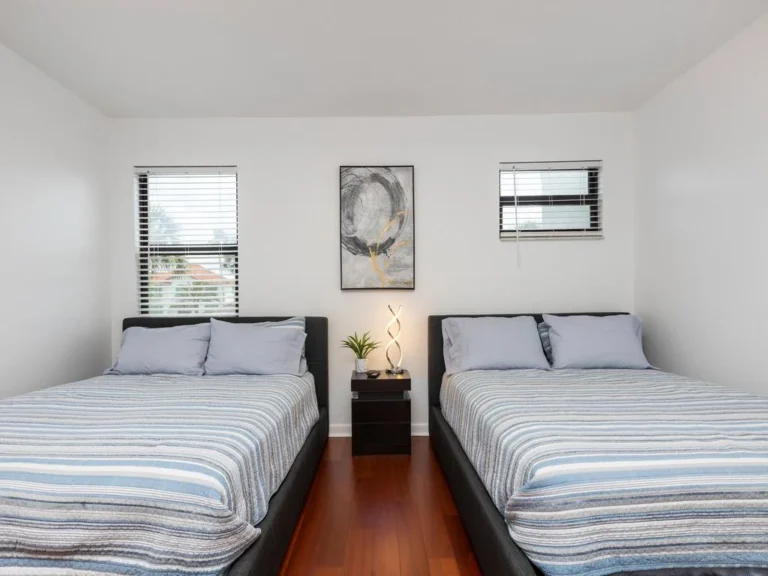 Natural light filters through dual windows above gray upholstered bed frames in the two-bed guest bedroom.