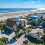 Aerial view of the beachside neighborhood with sandy dunes and ocean waves stretching along the coastline.