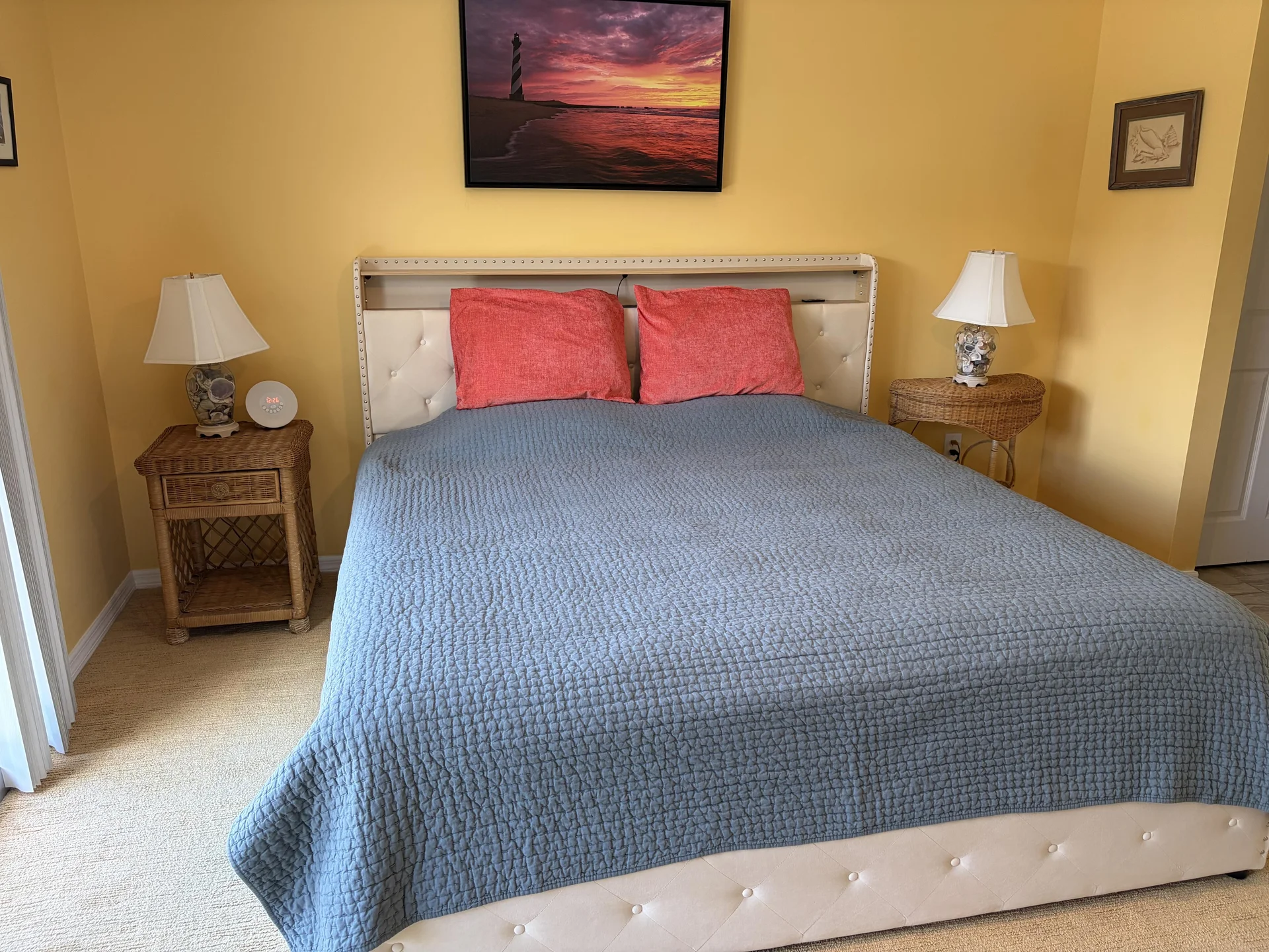 King bed with tufted white leather headboard, coral pillows, and wicker nightstands with decorative lamps.