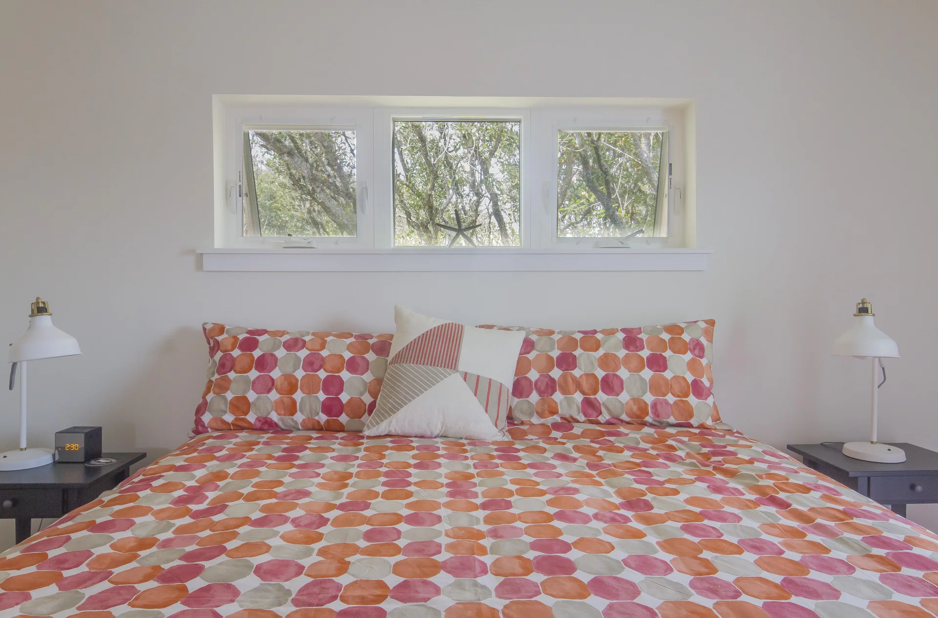 King bed with orange and pink geometric bedding beneath a trio of small rectangular windows.