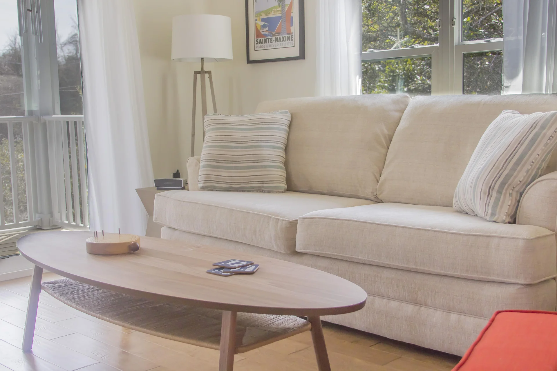 Light beige sofa with striped pillows faces a wooden oval coffee table on light hardwood floors.