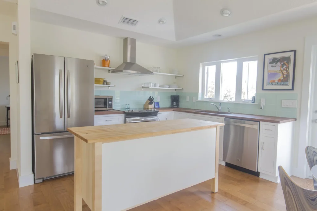 Butcher block island stands center in the kitchen with stainless steel appliances and pale aqua tile backsplash.