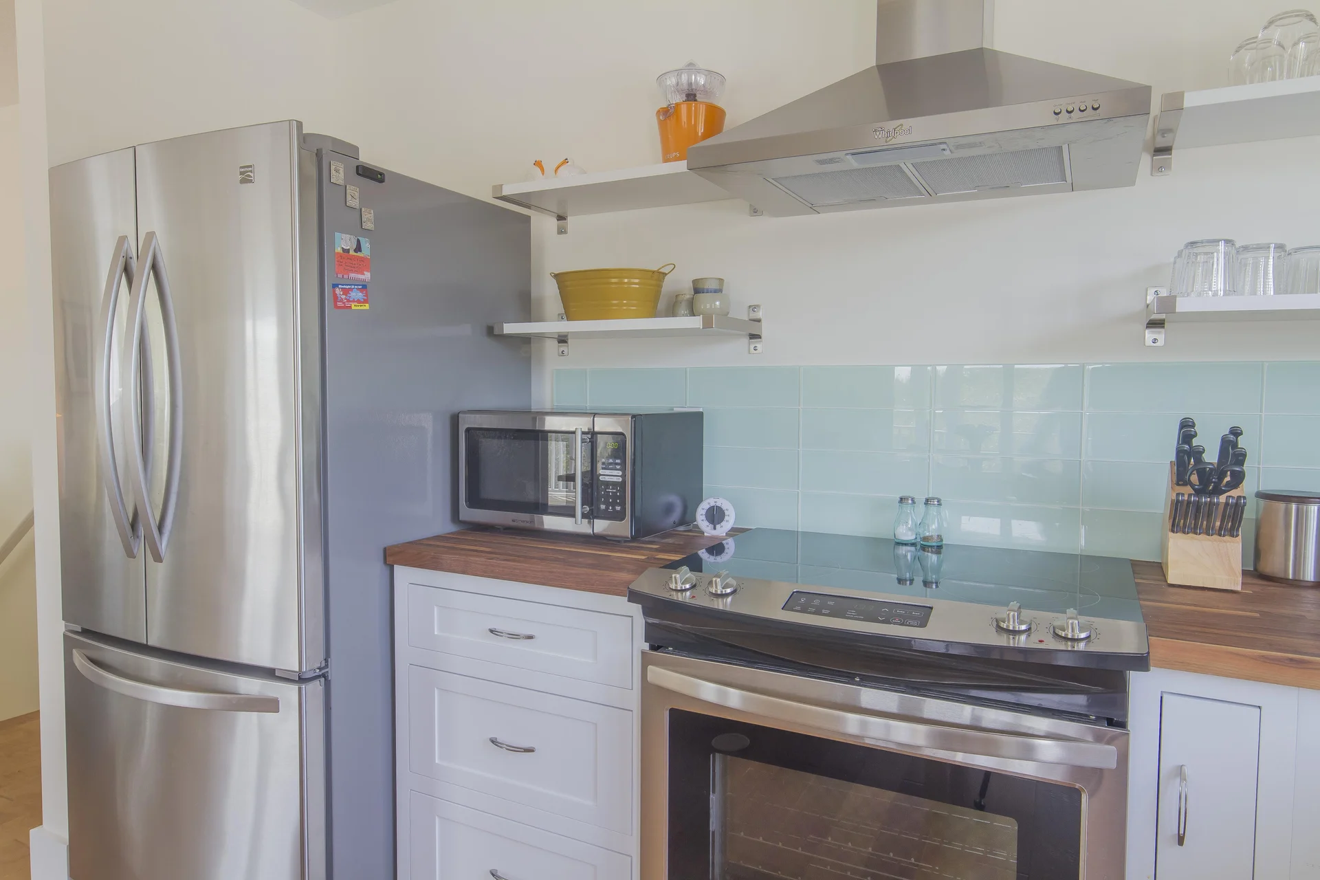 Stainless steel refrigerator and oven contrast with butcher block counters and pale aqua tile backsplash.