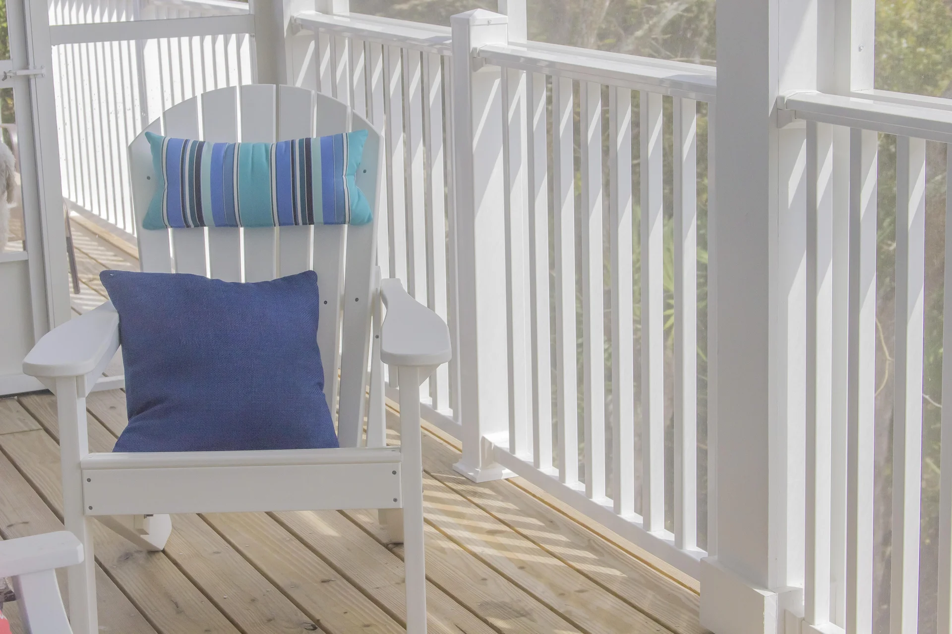Screened porch features white Adirondack chairs with blue pillows and light wood flooring.