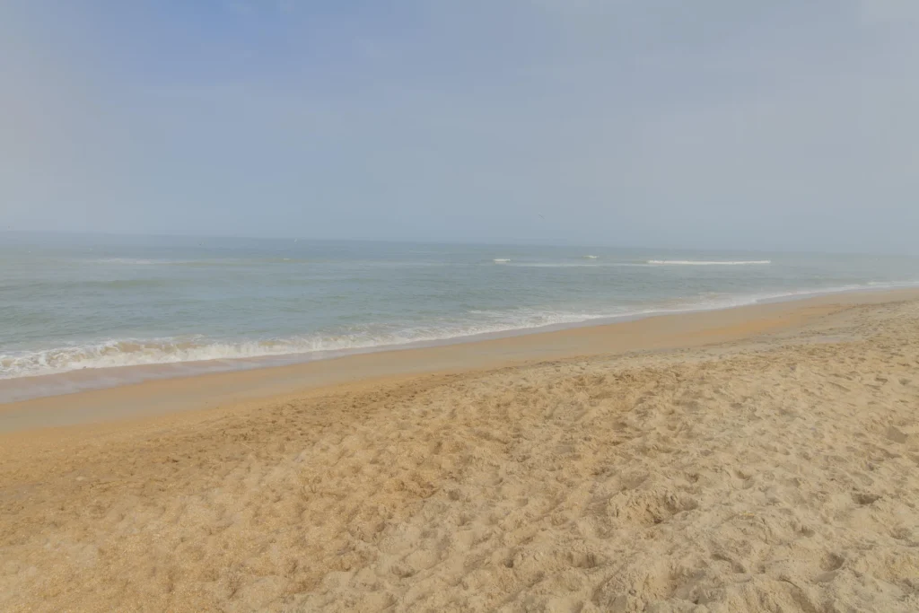 Sandy shoreline meets gentle waves under a pale blue sky on the nearby beach at Veterans Island.