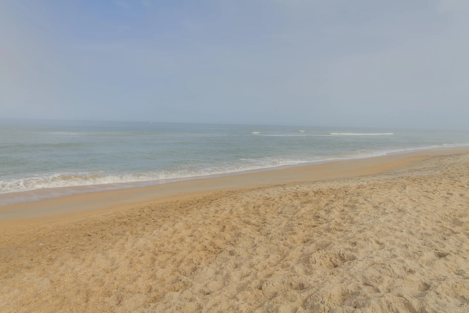 Sandy shoreline meets gentle waves under a pale blue sky on the nearby beach at Veterans Island.
