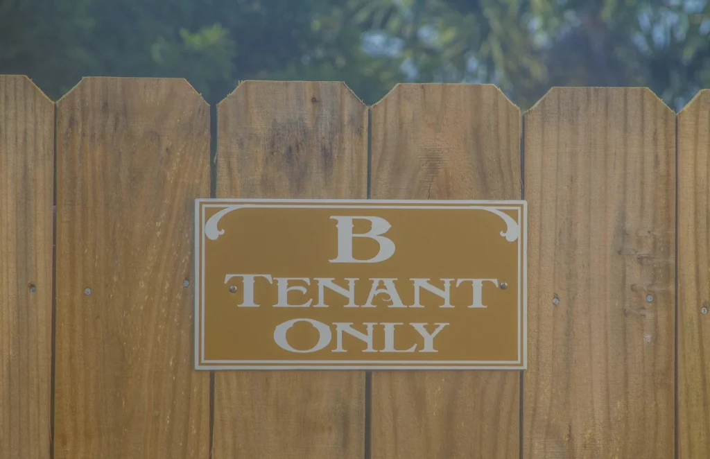 Yellow and white "B Tenant Only" sign mounted on a natural wood privacy fence with vertical planks.
