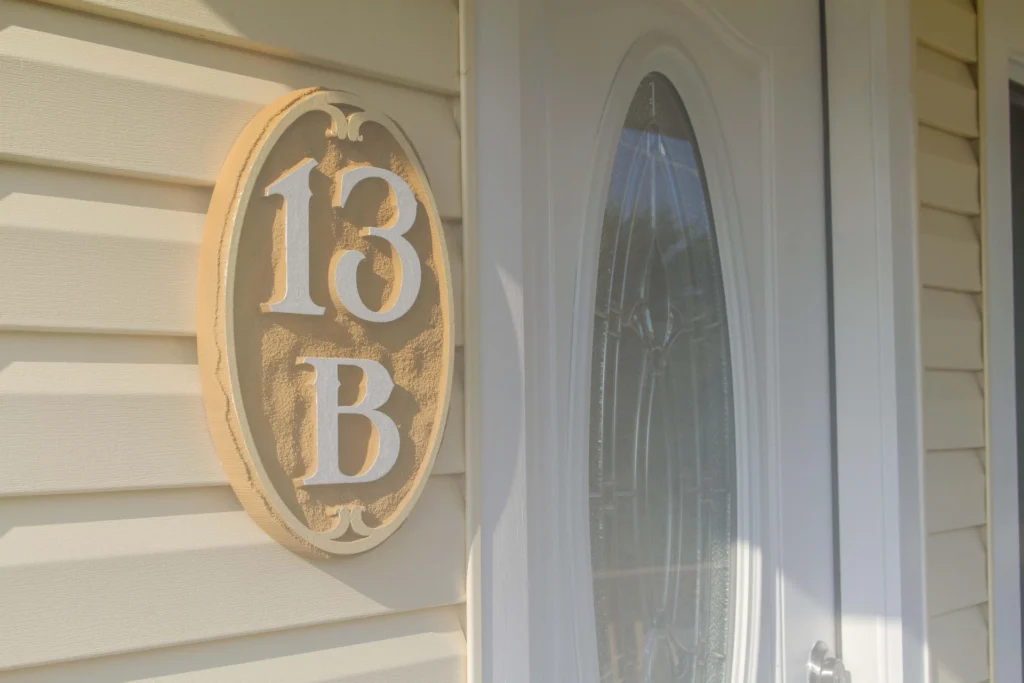 Close-up of textured beige siding beside a white front door with decorative oval glass panel.