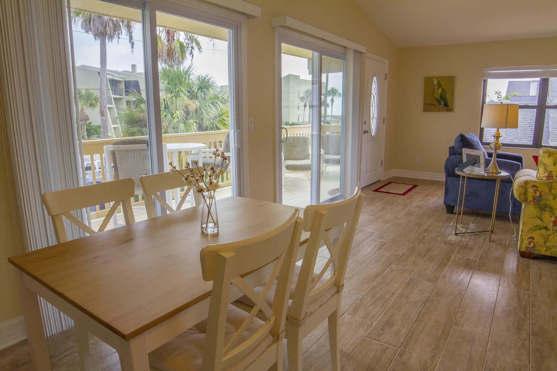 Dining area with light wood table, four white cross-back chairs, sliding glass doors opening to balcony.