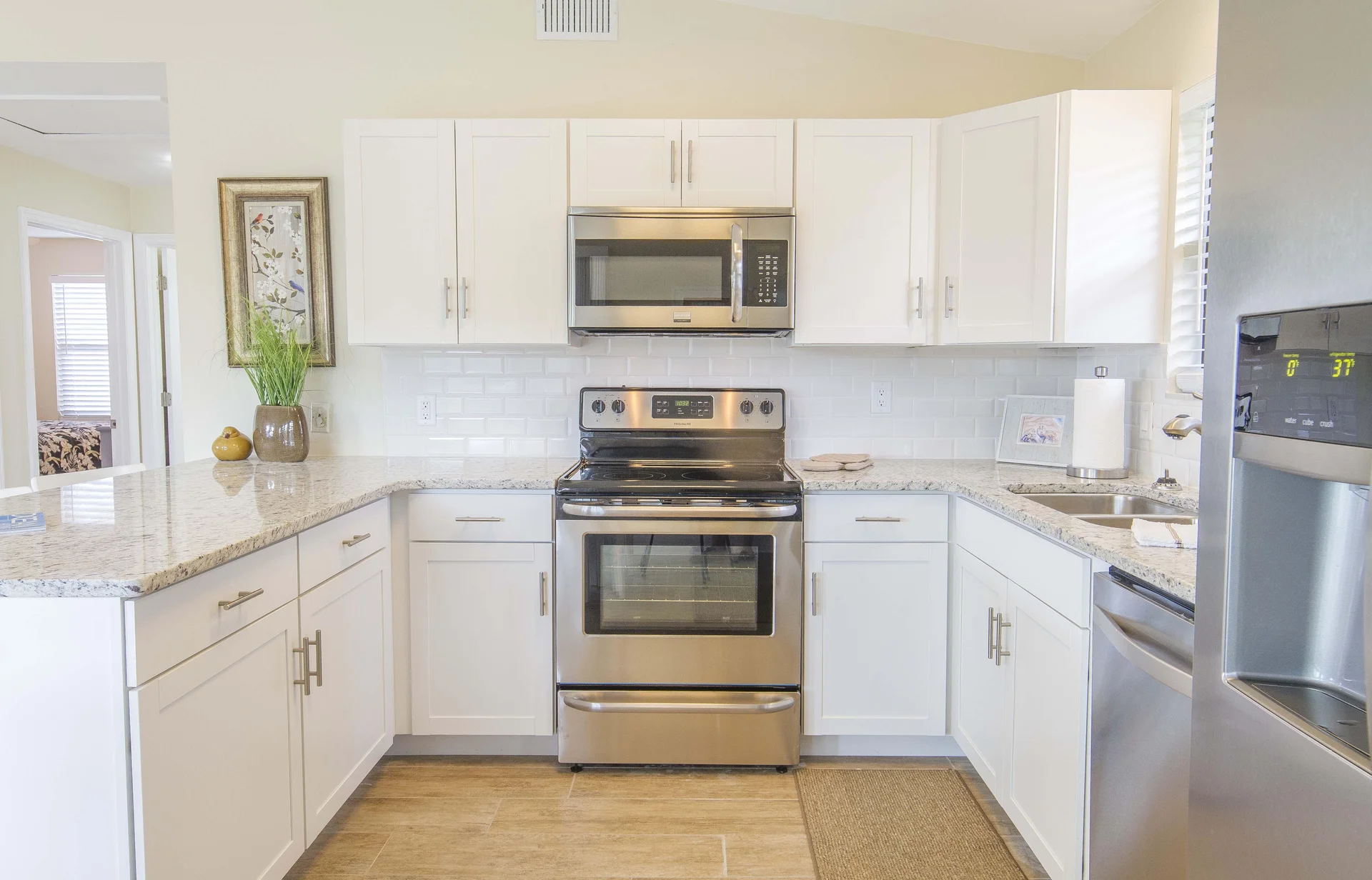 Stainless steel oven and microwave sit between white shaker cabinets and granite countertops in bright kitchen.