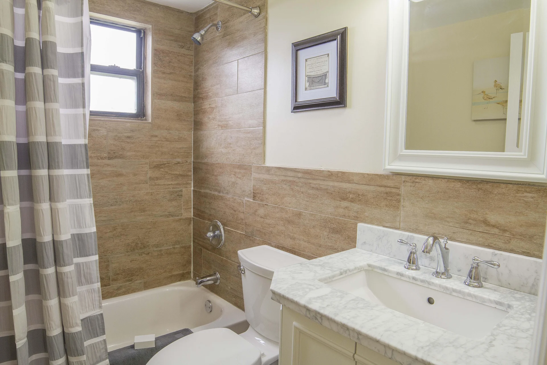 Bathroom with white porcelain tub, wood-look tile surround, gray-and-white checkered shower curtain, and marble countertop sink.