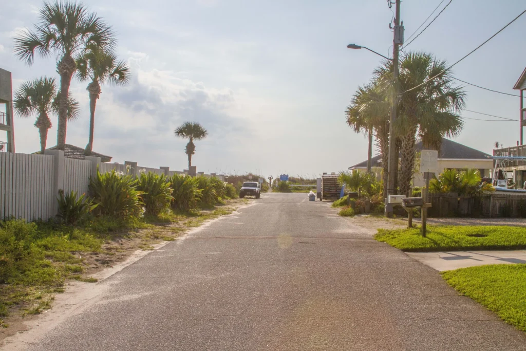 Quiet paved street lined with palm trees and greenery leading directly to sandy beach access.