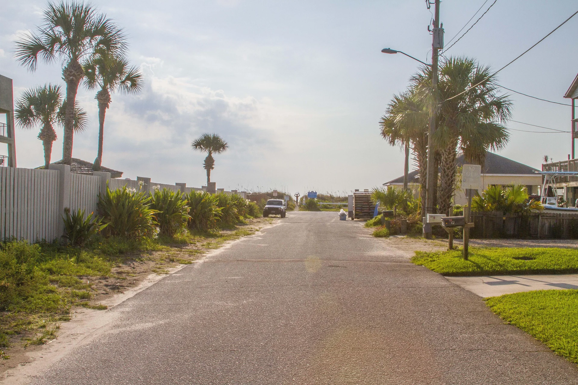 Quiet paved street lined with palm trees and greenery leading directly to sandy beach access.