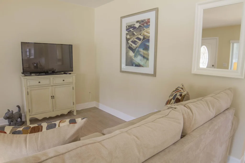 Flat-screen TV sits atop cream-colored wooden cabinet across from beige fabric sofa with patterned pillows.