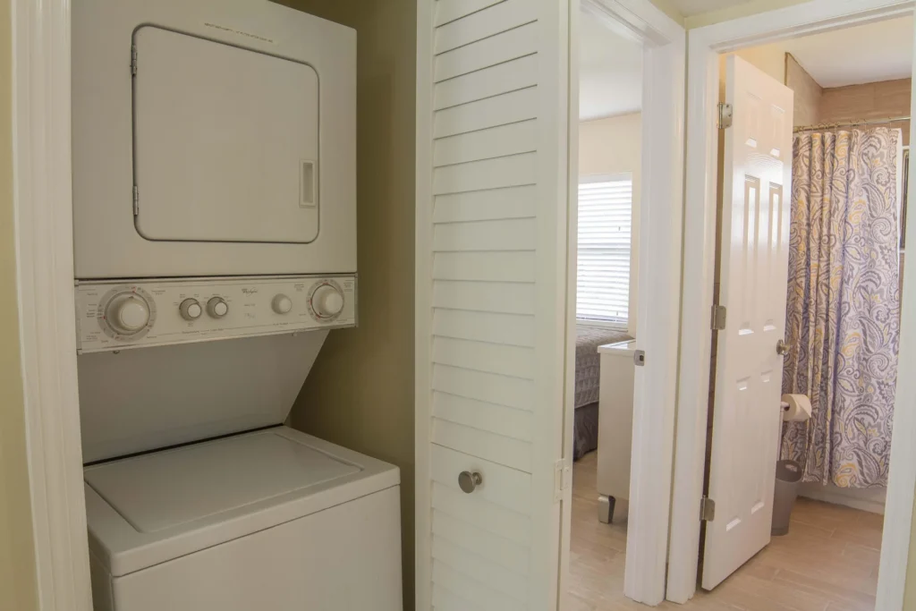 Stacked washer and dryer fit neatly behind white louvered doors beside the bathroom entrance.