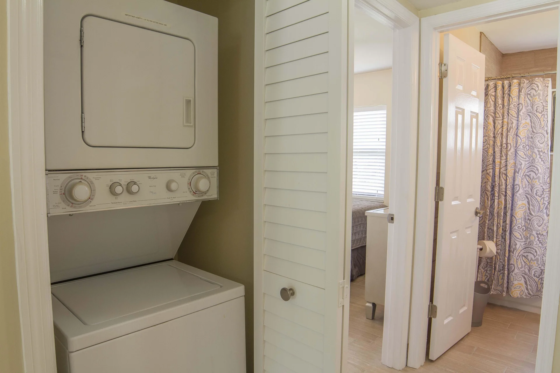 Stacked washer and dryer fit neatly behind white louvered doors beside the bathroom entrance.