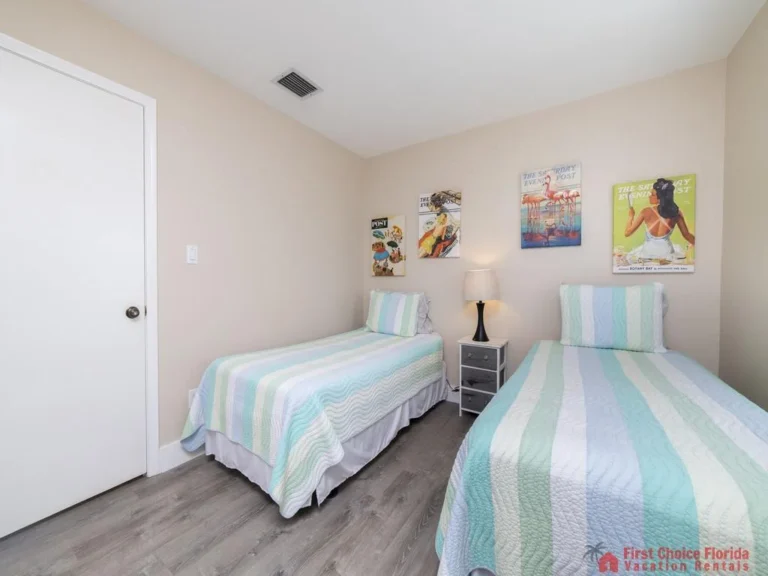 Light gray wood floors extend beneath twin beds with pastel striped quilts and a gray nightstand with lamp.