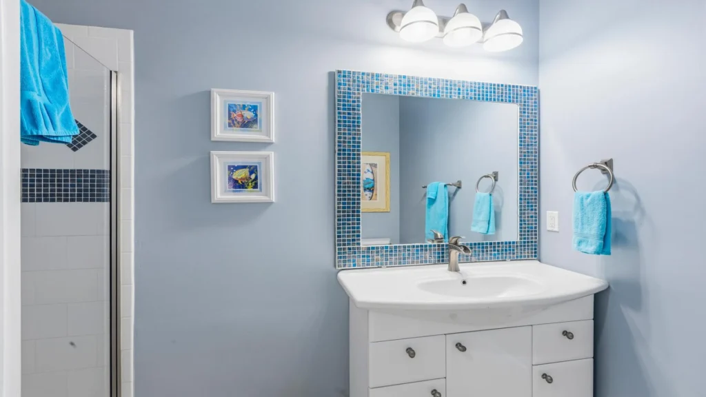 First-floor bathroom vanity with a mosaic blue tile mirror frame, brushed nickel faucet, and matching towel rings on soft blue walls.