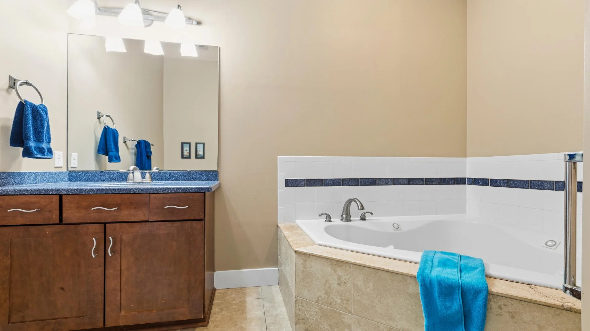 First-floor corner bathtub with beige tile surround and blue accent tile, next to a wooden vanity with blue countertop.