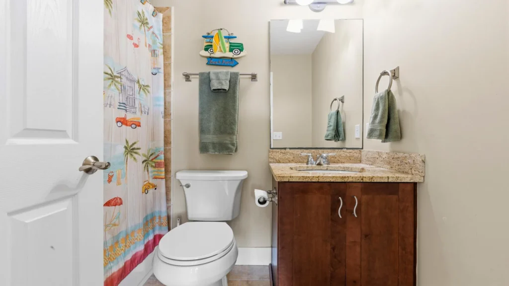 Bathroom with brown granite countertop, wood vanity, white toilet, and colorful beach-themed shower curtain.